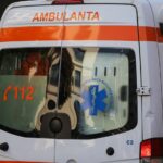 Rear view of a white ambulance with an orange stripe and 'AMBULANȚA' on the back, 112 printed in orange, and a blue Star of Life emblem visible in the window.