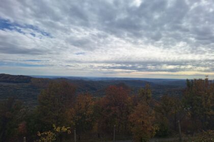 Hilly countryside with autumn trees under a cloudy sky; a fence runs along the foreground.