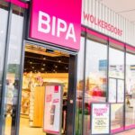 Front view of a BIPA cosmetics store with bright pink signs and glass storefronts, showing inside shelves and promotional displays.