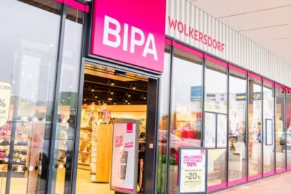 Front view of a BIPA cosmetics store with bright pink signs and glass storefronts, showing inside shelves and promotional displays.