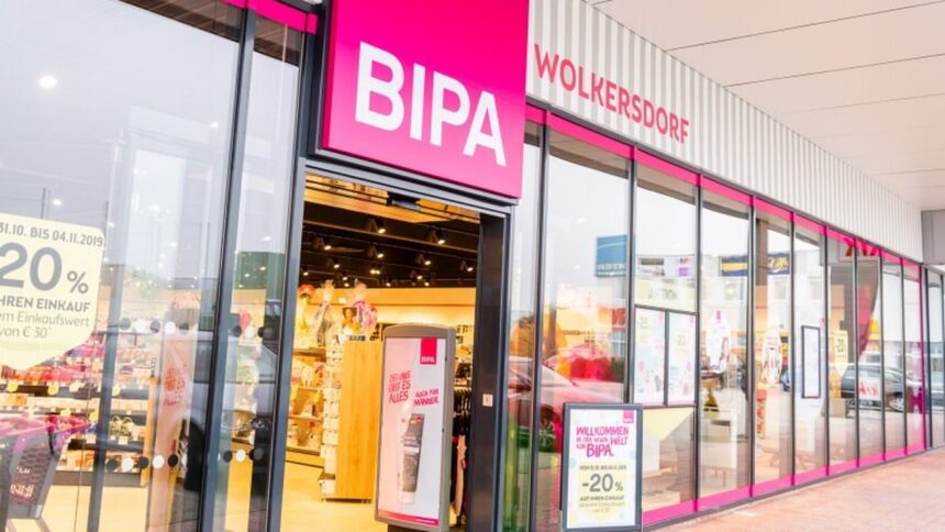 Front view of a BIPA cosmetics store with bright pink signs and glass storefronts, showing inside shelves and promotional displays.