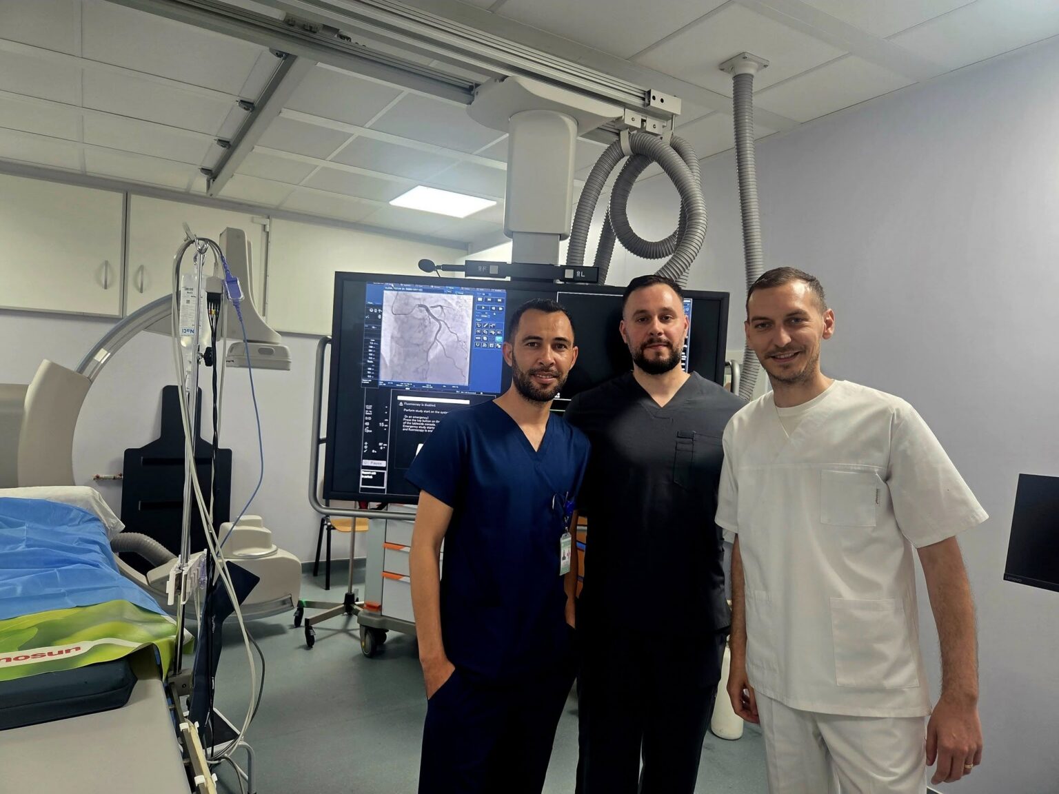 cardiologie spitalul slatina 709166184_122202887762436687_6887187739832324967_n medici - Jurnalul Olteniei – Știri din Craiova și Oltenia Three medical professionals in scrubs and a white coat stand in an operating room beside a large monitor displaying medical images.