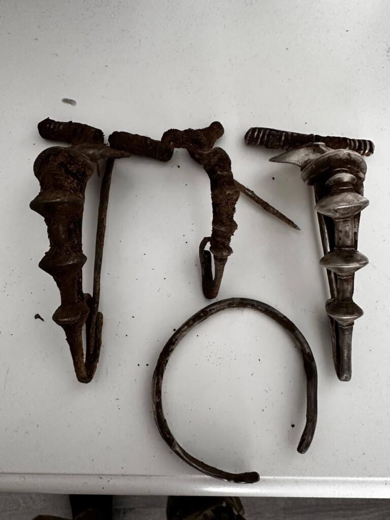 Several rusted metal hardware pieces—a pair of threaded posts, a curved hook, and a circular ring on a white surface.