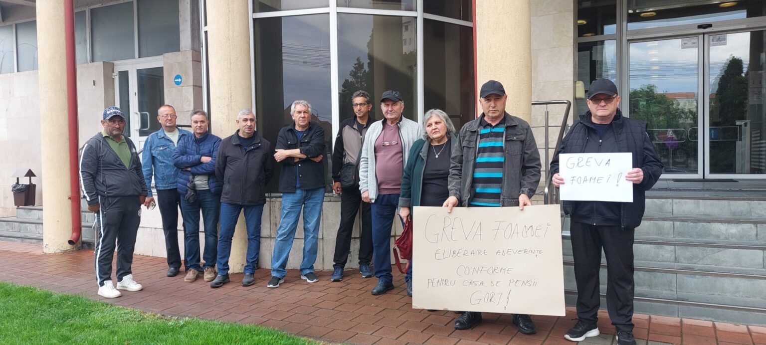 Group of people standing in a line outside a building, holding hunger-strike signs.
