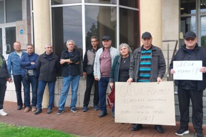 Group of people standing in a line outside a building, holding hunger-strike signs.