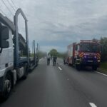 Emergency scene on a two-lane road with a large truck on the left and a red fire truck on the right; responders stand in the road.