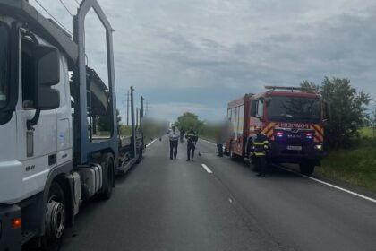 Emergency scene on a two-lane road with a large truck on the left and a red fire truck on the right; responders stand in the road.