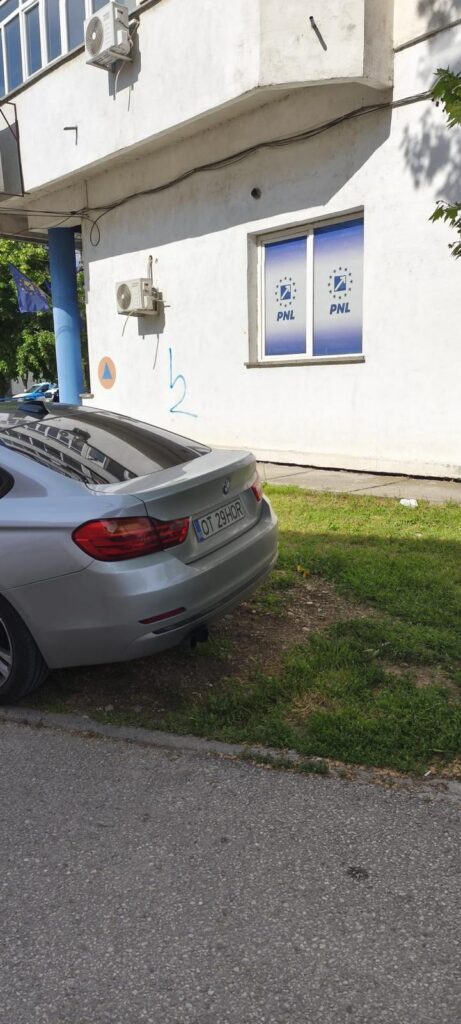 Silver BMW parked on a grassy verge beside a white building with PNL banners in the window. The scene includes air conditioners and a blue flag.