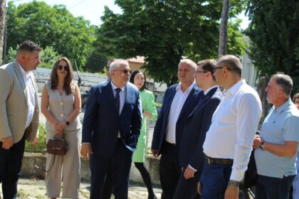 Group of professionals in business attire standing outdoors near a fence, engaged in conversation on a sunny day.
