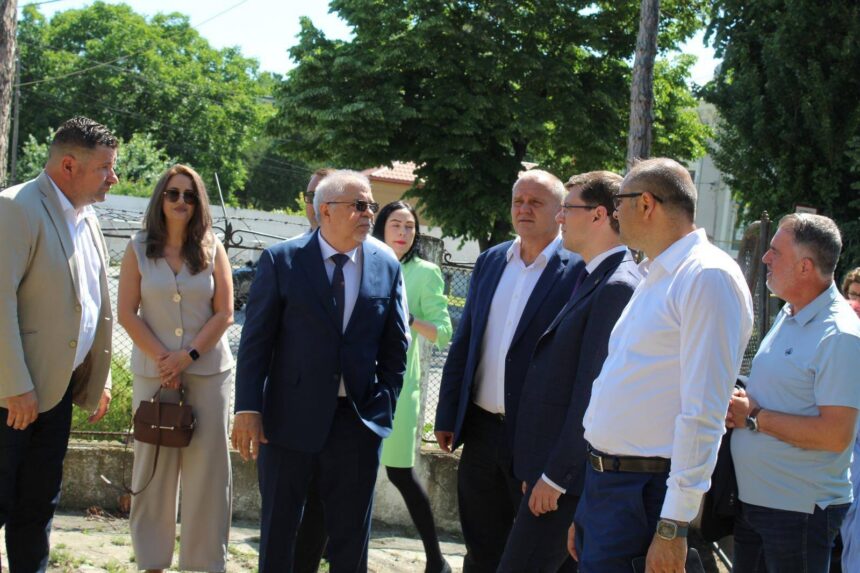 Group of professionals in business attire standing outdoors near a fence, engaged in conversation on a sunny day.