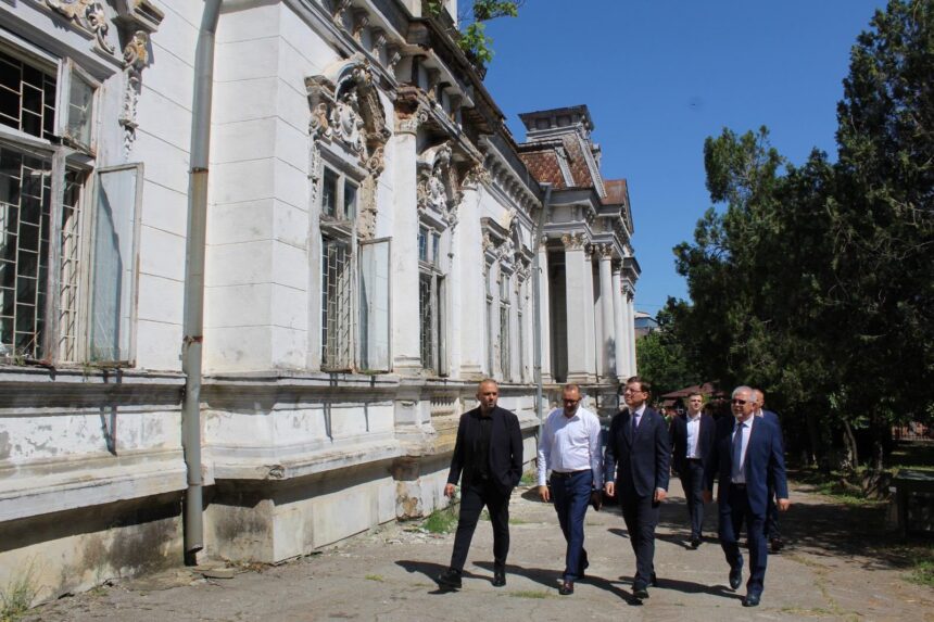 Group of men in business attire walking along the side of an old ornate white building with carved windows under a clear blue sky.