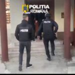 Romanian police officers in tactical vests walking toward a building entrance, with 'POLITIA' on their backs.