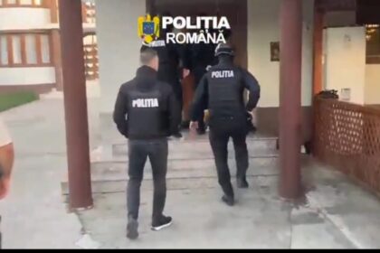 Romanian police officers in tactical vests walking toward a building entrance, with 'POLITIA' on their backs.