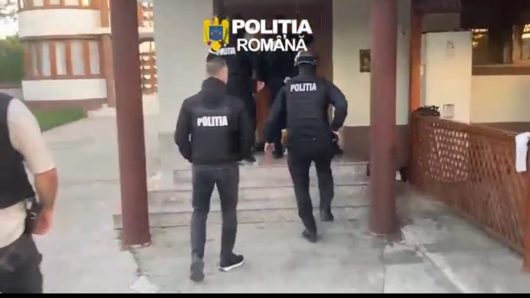 Romanian police officers in tactical vests walking toward a building entrance, with 'POLITIA' on their backs.