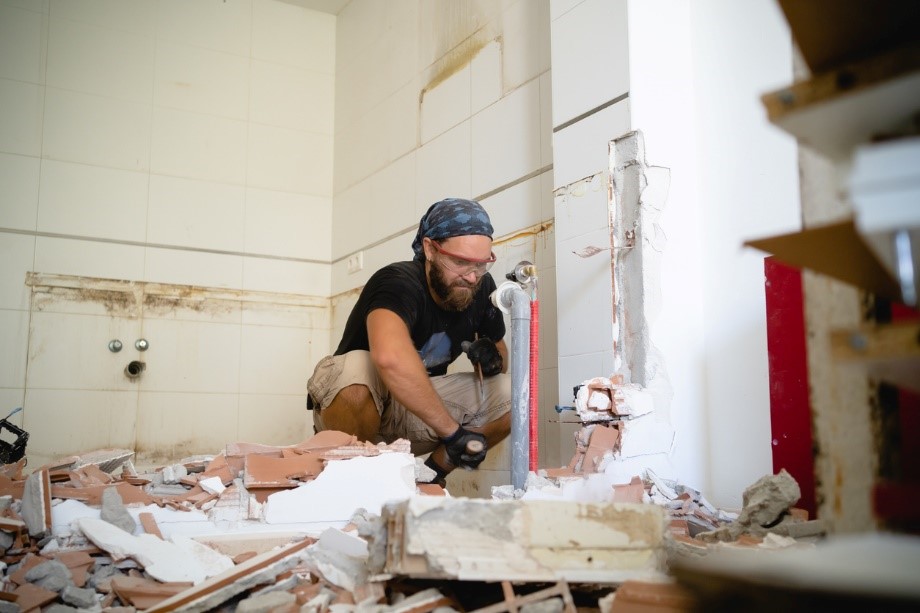 Construction worker with a bandana chiseling through bricks in a partially demolished room filled with rubbleing debris on the floor