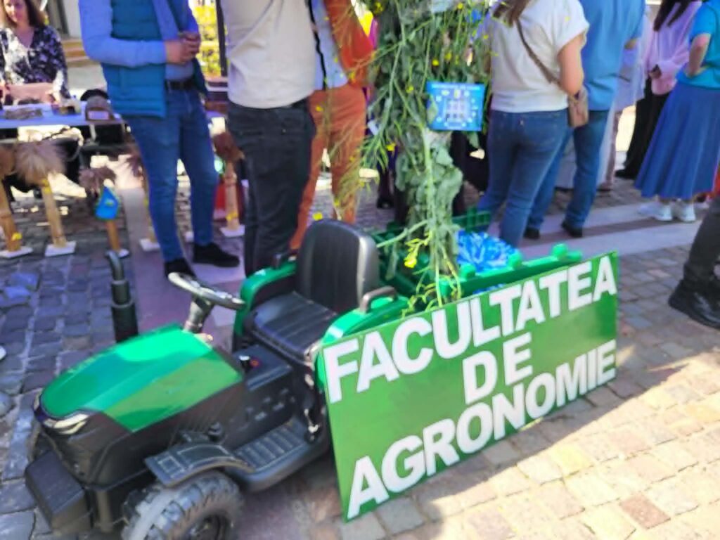 People gathered at an outdoor event around a green booth banner with large white text; a green vehicle/scooter is in the foreground.