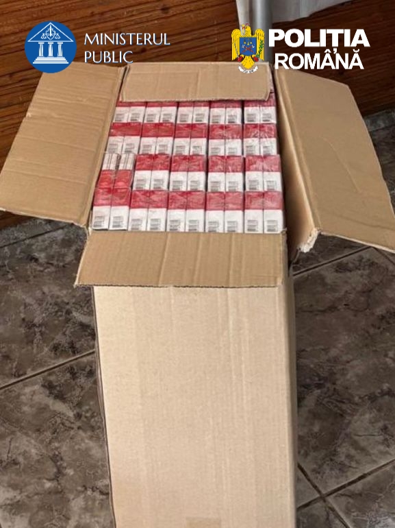 Open cardboard box filled with rows of red-and-white cigarette packs; ministry and Romanian police logos visible in the top corners.