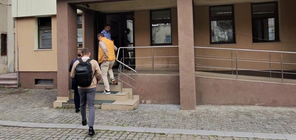 People with backpacks walking up concrete steps to a building entrance with a ramp on the side.