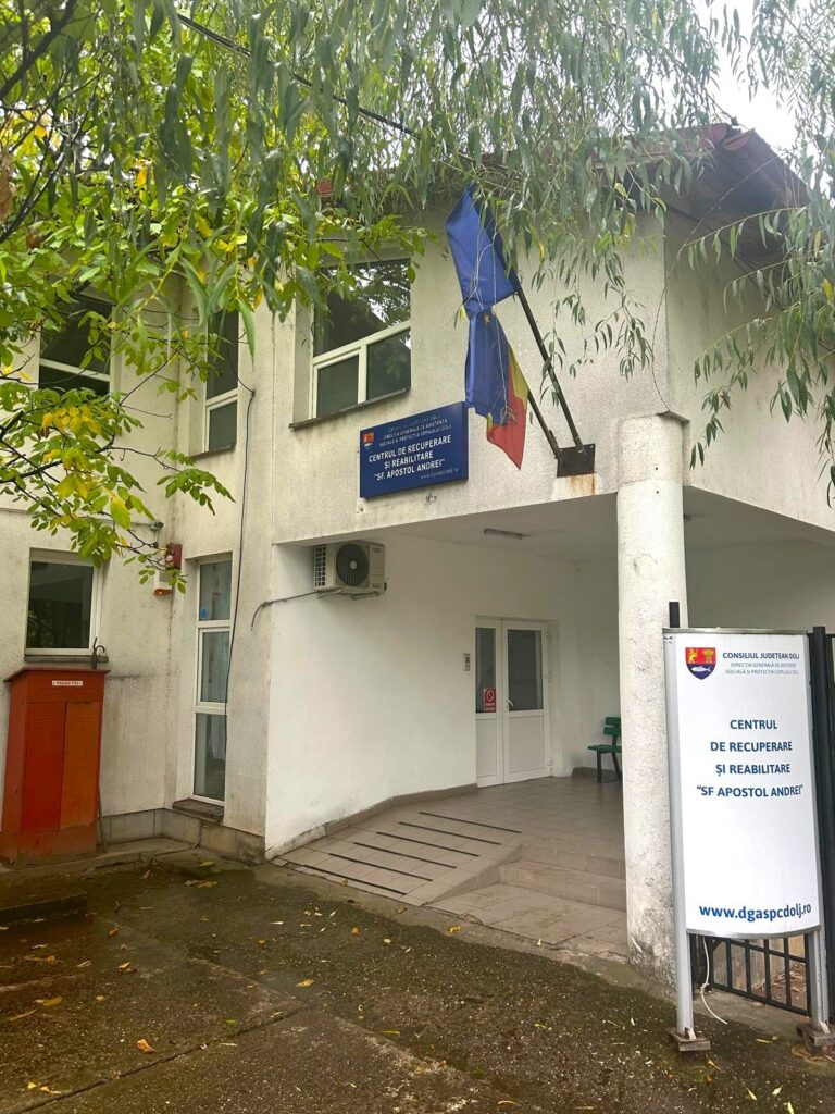 Entrance to the Center for Recovery and Rehabilitation 'Sf Apostol Andrei' with a blue sign and flags above the doorway.