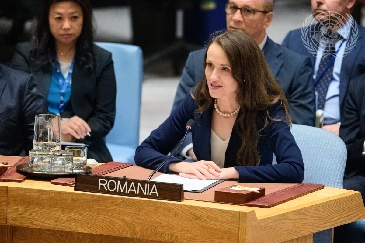 Romanian delegate woman speaks into a desk microphone at a United Nations–style meeting, Romania nameplate in foreground.