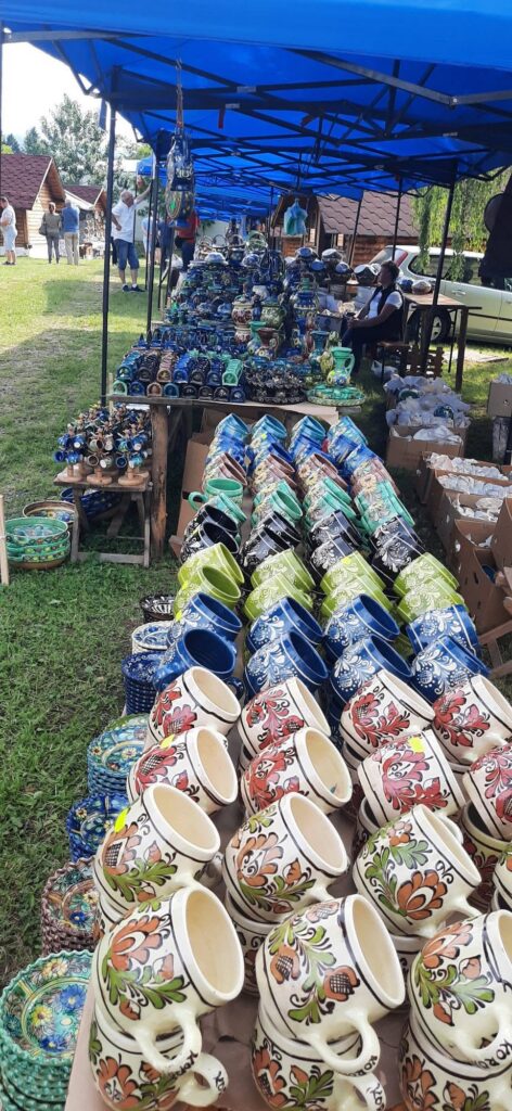 Outdoor market stall selling colorful ceramic mugs and pots under blue canopies.