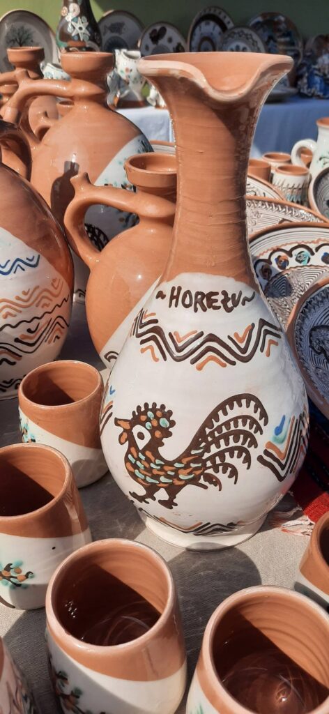 Display of terracotta and white pottery with rooster and geometric designs at a market stall.
