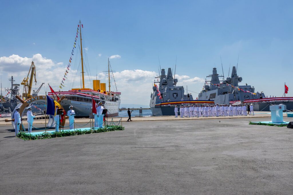 - Jurnalul Olteniei – Știri din Craiova și Oltenia Naval ceremony on a pier with two large warships and sailors in white uniforms lined up under a clear blue sky, with flags and bunting.