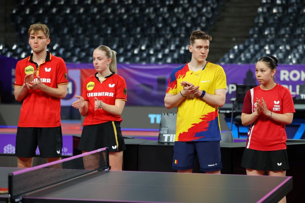- Jurnalul Olteniei – Știri din Craiova și Oltenia Four table tennis players stand side by side at a table, clapping in a stadium with purple banners in the background.