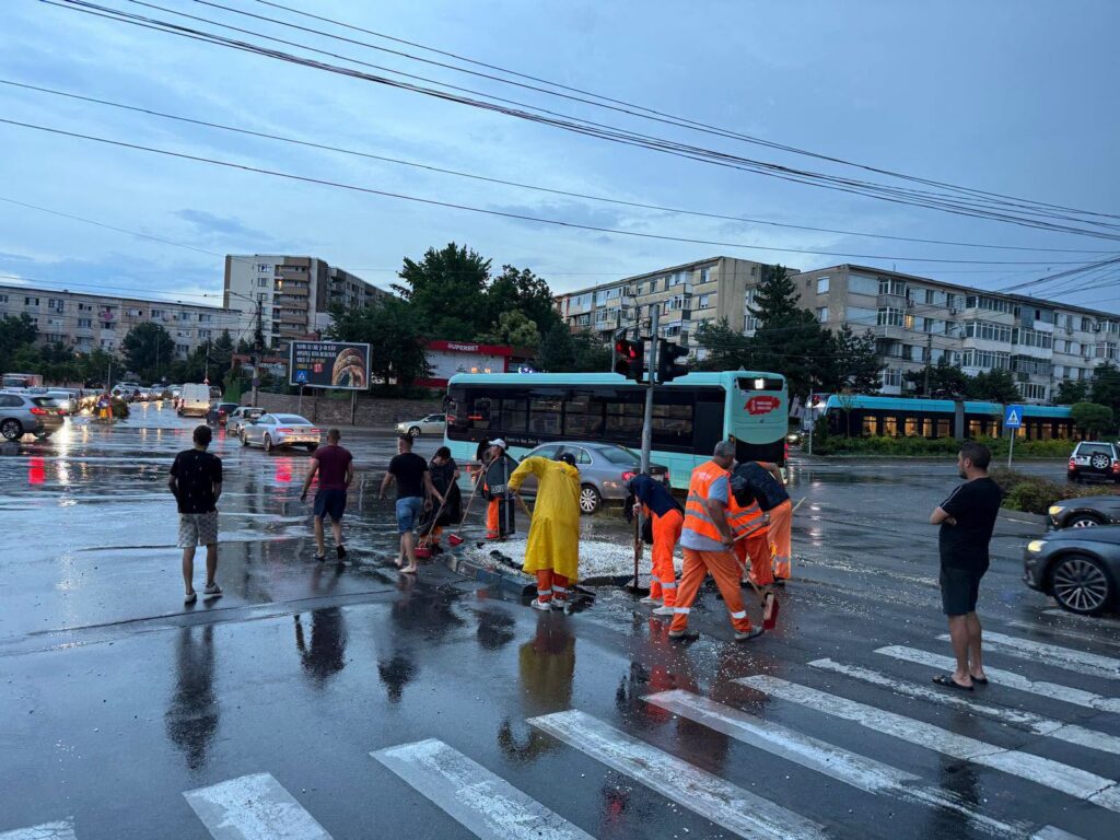 responders in orange gear and a yellow raincoat shoveling water and debris at a flooded city intersection at dusk