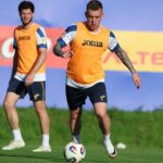 Soccer players in orange training bibs on a green field, central player dribbling a ball during practice.
