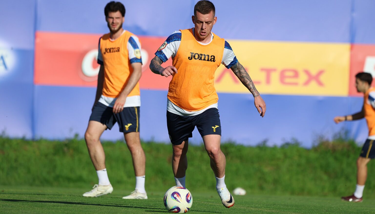 Soccer players in orange training bibs on a green field, central player dribbling a ball during practice.