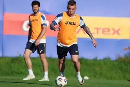 Soccer players in orange training bibs on a green field, central player dribbling a ball during practice.