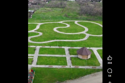 Aerial view of a park with winding white gravel paths around a small hexagonal gazebo and neat grassy plots with benches.