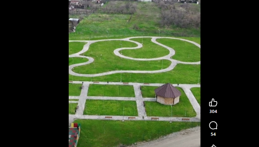 Aerial view of a park with winding white gravel paths around a small hexagonal gazebo and neat grassy plots with benches.