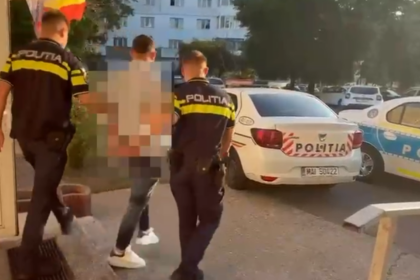 Three police officers in dark uniforms with yellow stripes detain a pixelated individual outside a building, beside a white police car labeled POLITIA. A residential area is in the background.