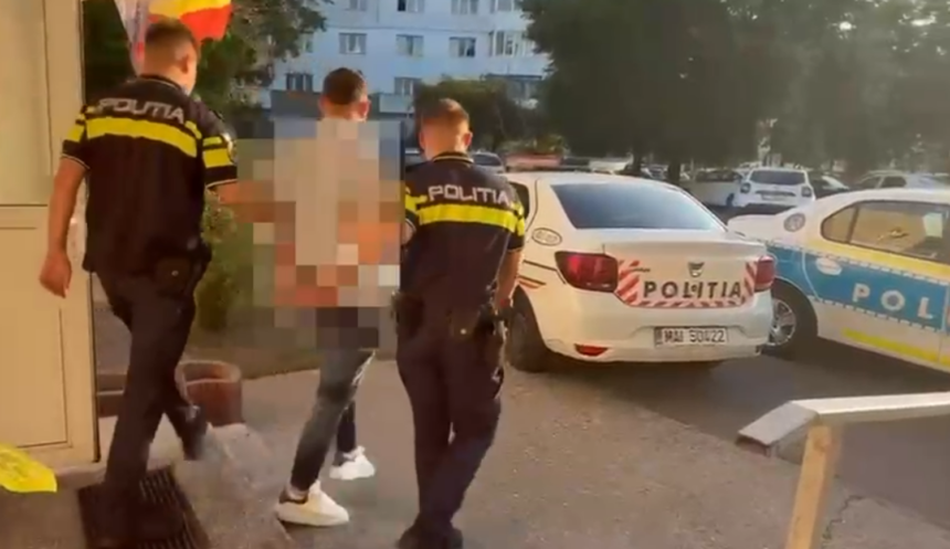 Three police officers in dark uniforms with yellow stripes detain a pixelated individual outside a building, beside a white police car labeled POLITIA. A residential area is in the background.