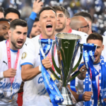 Soccer players celebrate with a large trophy and blue ribbons after winning a championship