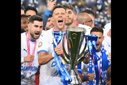 Soccer players celebrate with a large trophy and blue ribbons after winning a championship