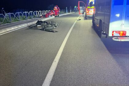 Nighttime road accident scene with a damaged Yamaha motorcycle on the road and emergency responders nearby near a barrier fence on the left side of the road.