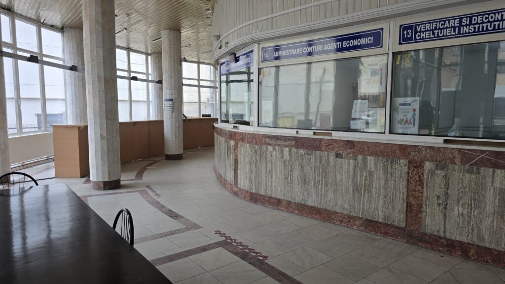 Interior of a government service hall with curved marble counter and glass windows; empty desks and pillars in view.
