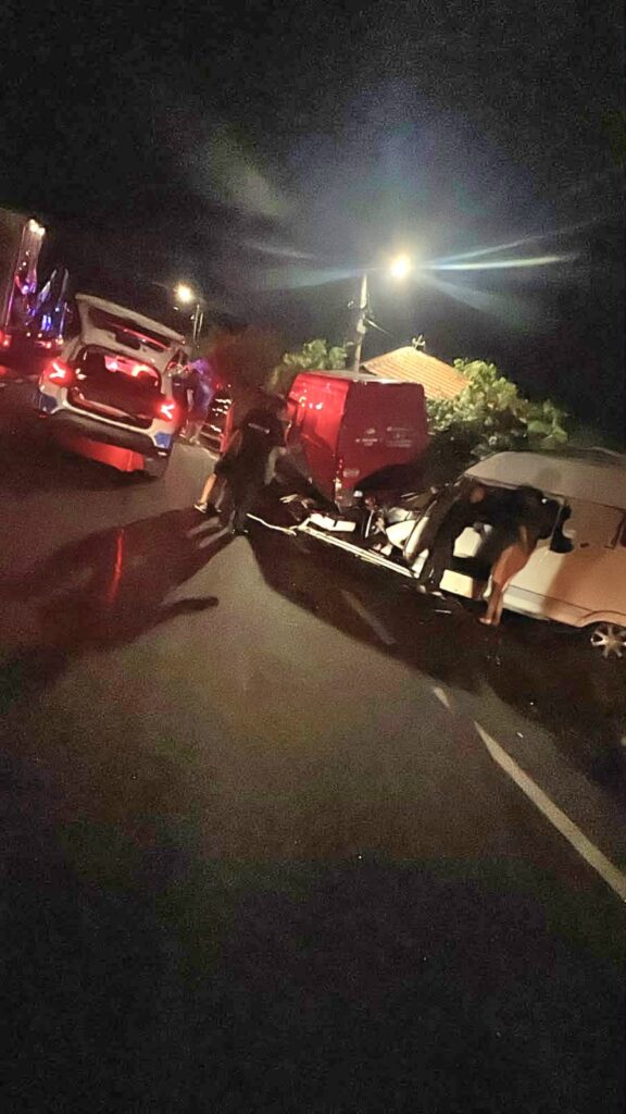 Nighttime crash on a street with several damaged vehicles and bystanders examining the scene.