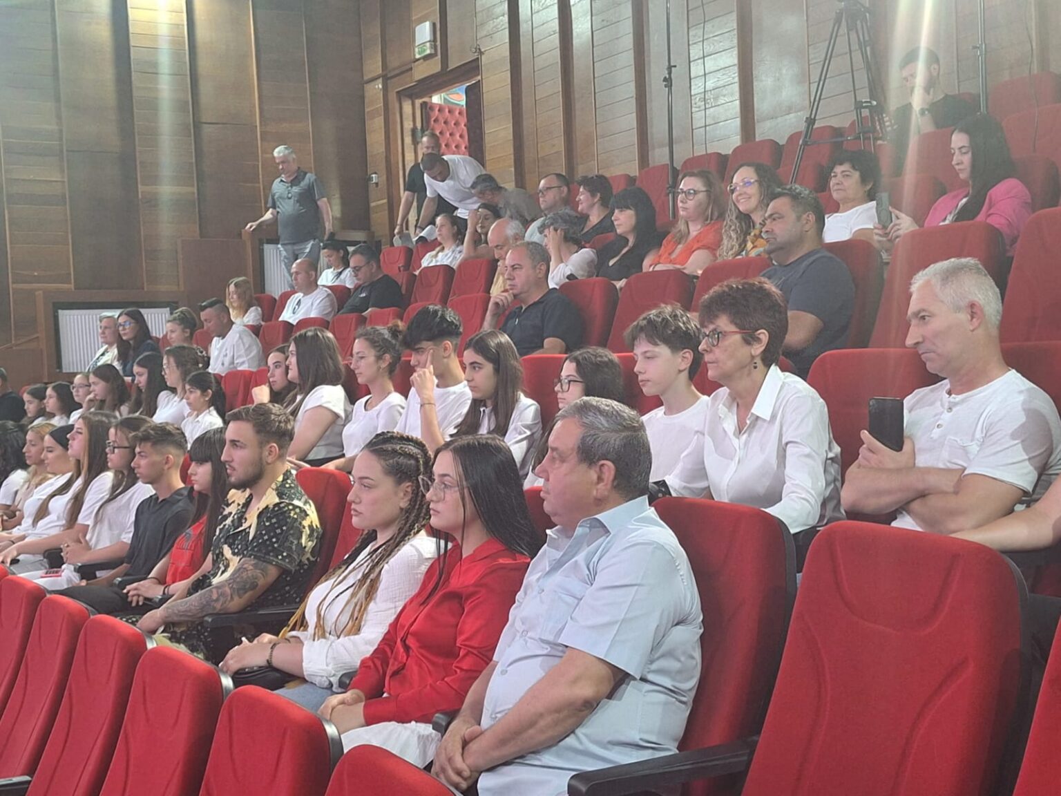 WhatsApp Image 2026-06-09 at 134459 1 - Jurnalul Olteniei – Știri din Craiova și Oltenia Audience seated in red theater chairs, watching an event; mix of students and adults in a lecture-room setting.