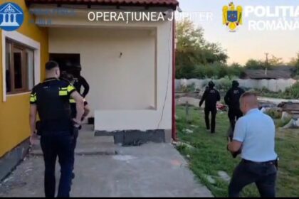 Police officers in black uniforms entering a yellow house during a raid, labeled 'OPERATIUNE' with Romanian Police logos visible outside.