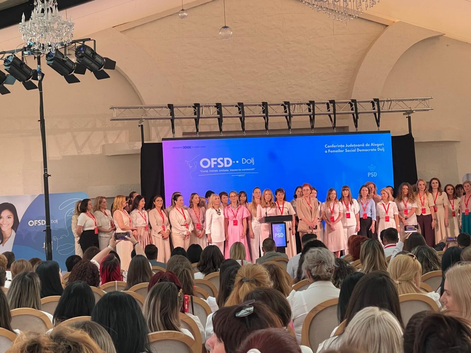 Alexandra Presură este noua șefă a OFSD Dolj - Jurnalul Olteniei – Știri din Craiova și Oltenia Group of women on a stage at a conference, standing in a row in front of a blue backdrop with OFSD Dolj branding. Audience seated in front.