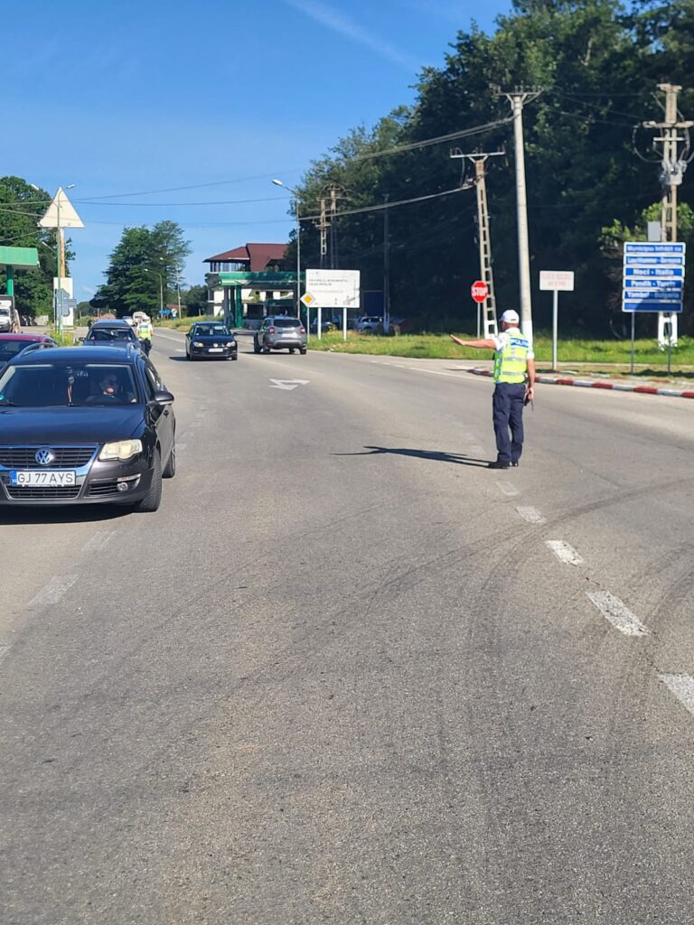 Police officer in reflective vest directing traffic on a sunny street with cars passing by.
