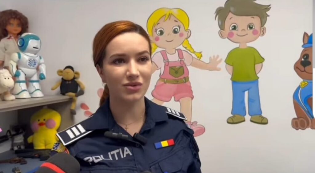 Female police officer in uniform giving an interview in a children's playroom with toys and cartoon characters on the wall.