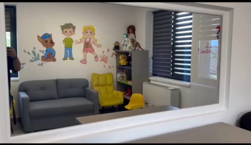 Playroom with a gray sofa, bright yellow chairs, and a cartoon wall mural of children and a dog, plus toy shelves in the corner.