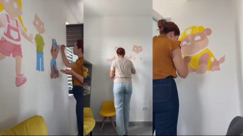 Two adults painting large colorful cartoon characters on white walls in a playroom, with yellow chairs nearby.