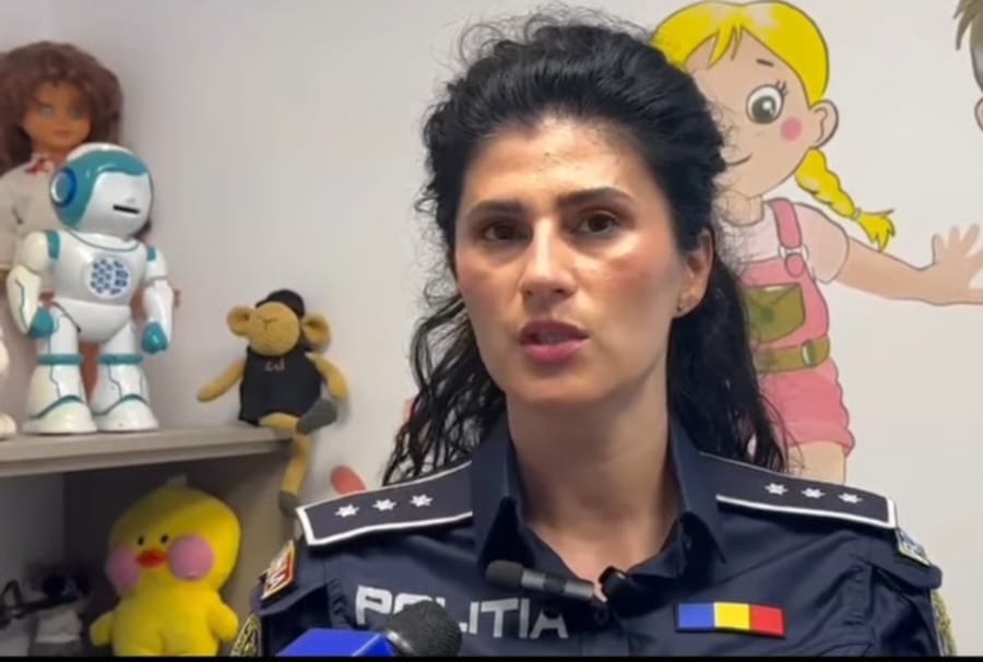 Police officer in uniform speaks during an interview, with toys on a shelf behind her.