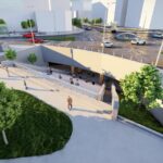 Sunken entrance to an underground transit station with stairs and ramps, pedestrians, and surrounding trees in a modern city plaza.